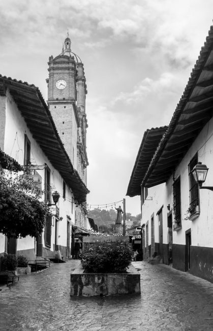 Fotomural Vista en blanco y negro de una torre del reloj histórica y calle de adoquines en un encantador pueblo mexicano.