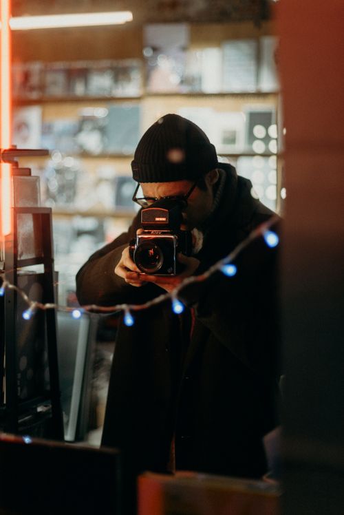 Free A photographer uses a vintage camera inside a cozy, softly lit room with decorative string lights. Stock Photo