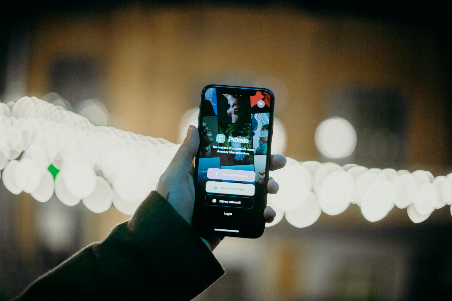 A hand holding a smartphone displaying an app login screen with a vibrant bokeh light background.