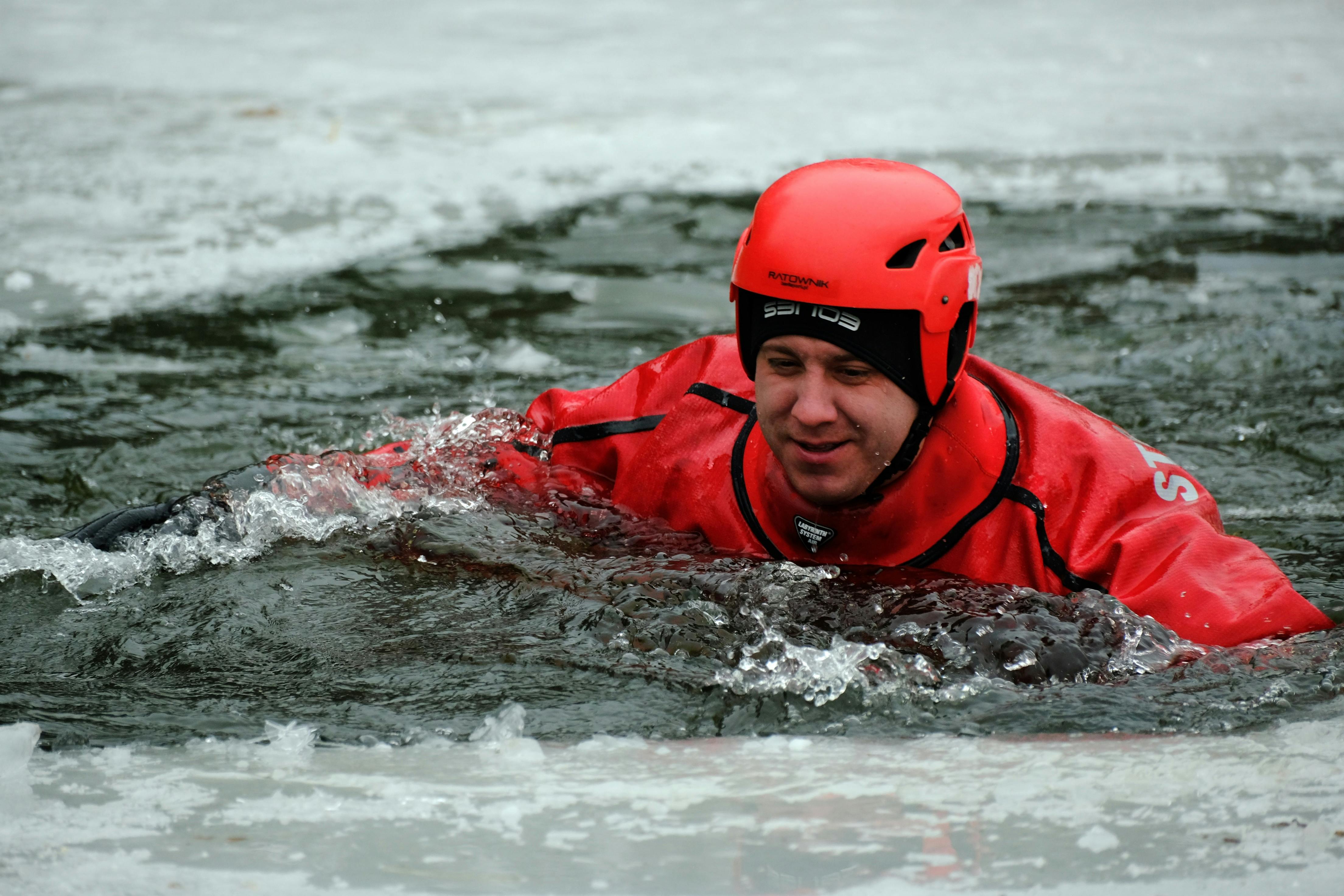 A person in red safety gear practicing ice rescue techniques during winter outdoors.