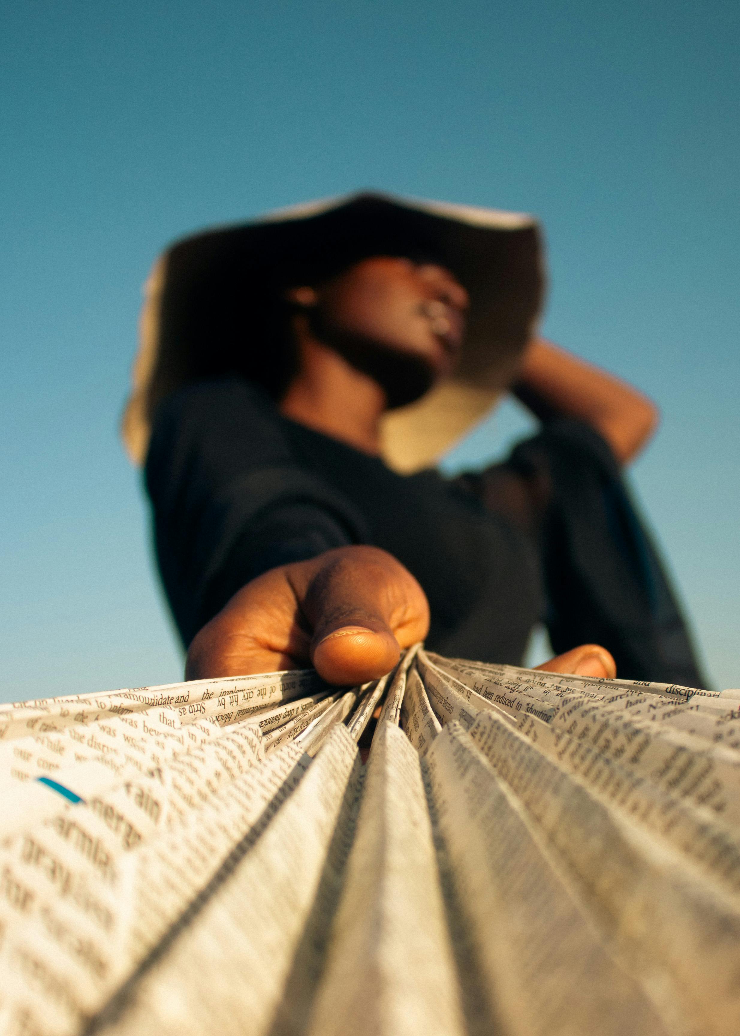 Free Close-up of a woman holding a newspaper with a blurred outdoor background, emphasizing style and interest. Stock Photo