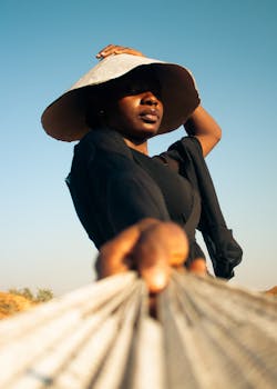 Striking portrait of a woman in a wide-brimmed hat under the sun with a relaxed pose and intense gaze.