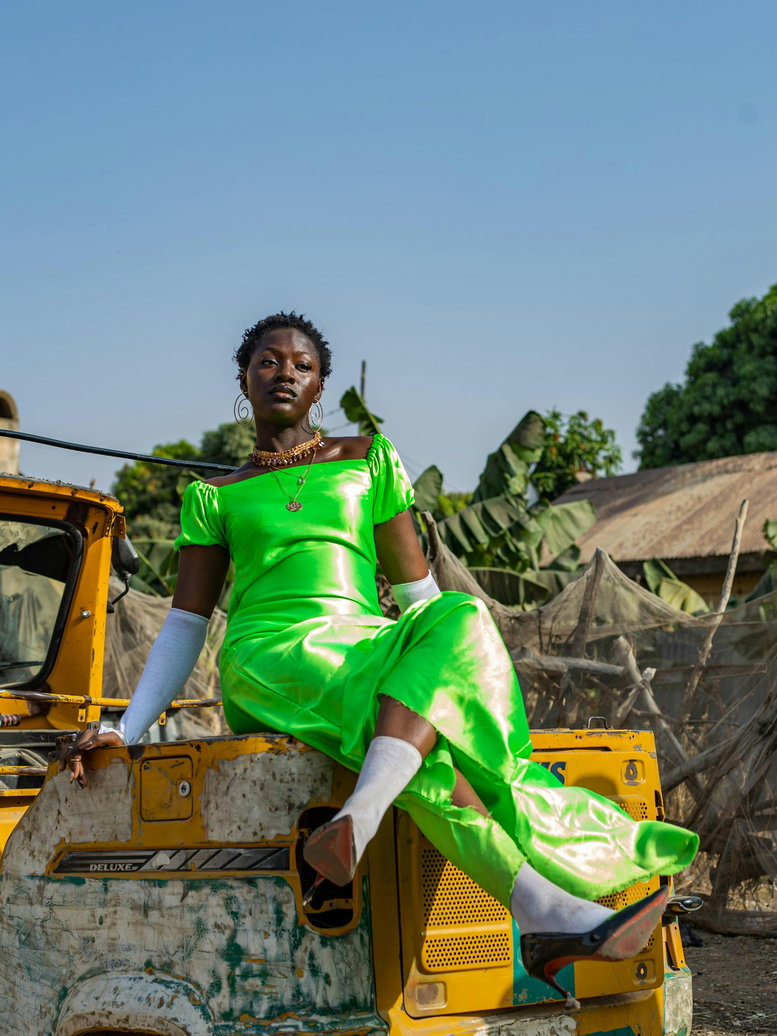 A stunning portrait of a woman in a neon green dress sitting on construction equipment.