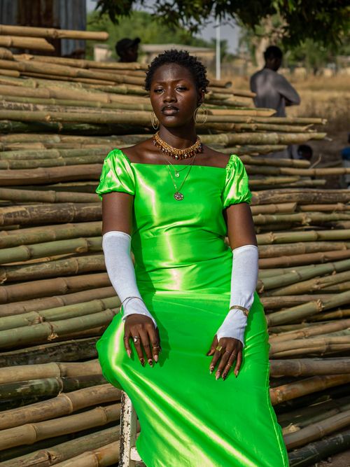 Free Portrait of a woman in a bright green dress sitting confidently against a bamboo background outdoors. Stock Photo