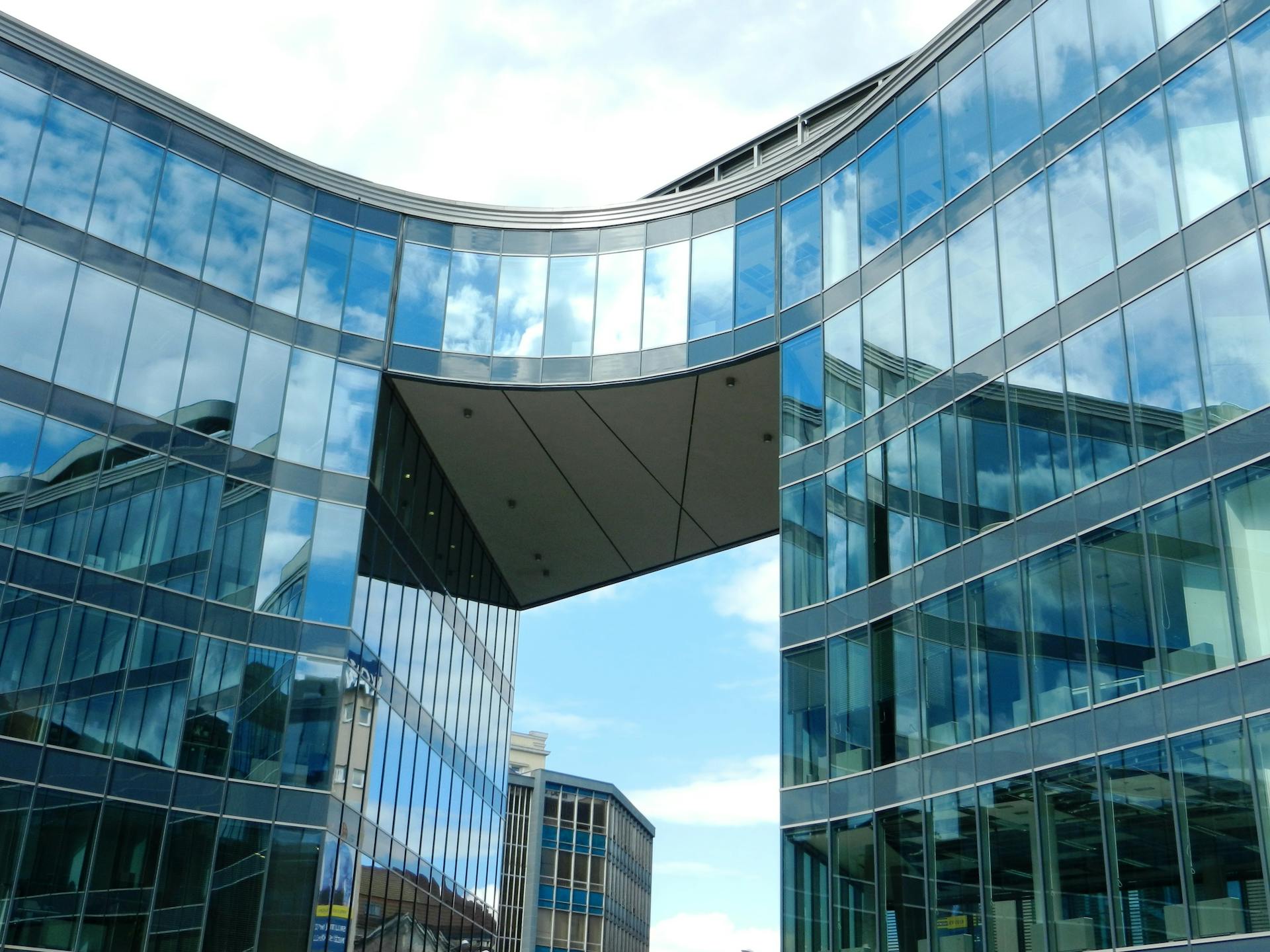 Modern glass office building with unique design reflecting blue sky.