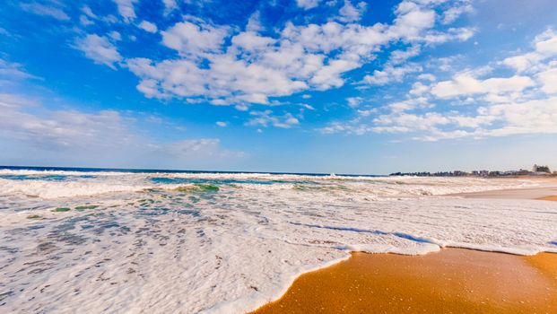Vibrant beach scene with waves crashing on shore under a clear blue sky.