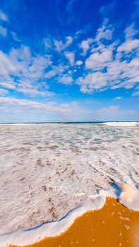 A tranquil beachfront with foamy waves under a vivid blue sky, ideal for relaxation themes.