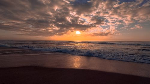 Free Beautiful sunset over a tranquil beach with dramatic clouds and gentle waves. Stock Photo