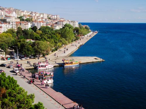 Free A lively coastal boardwalk with boats, trees, and urban skyline against a deep blue sea. Stock Photo