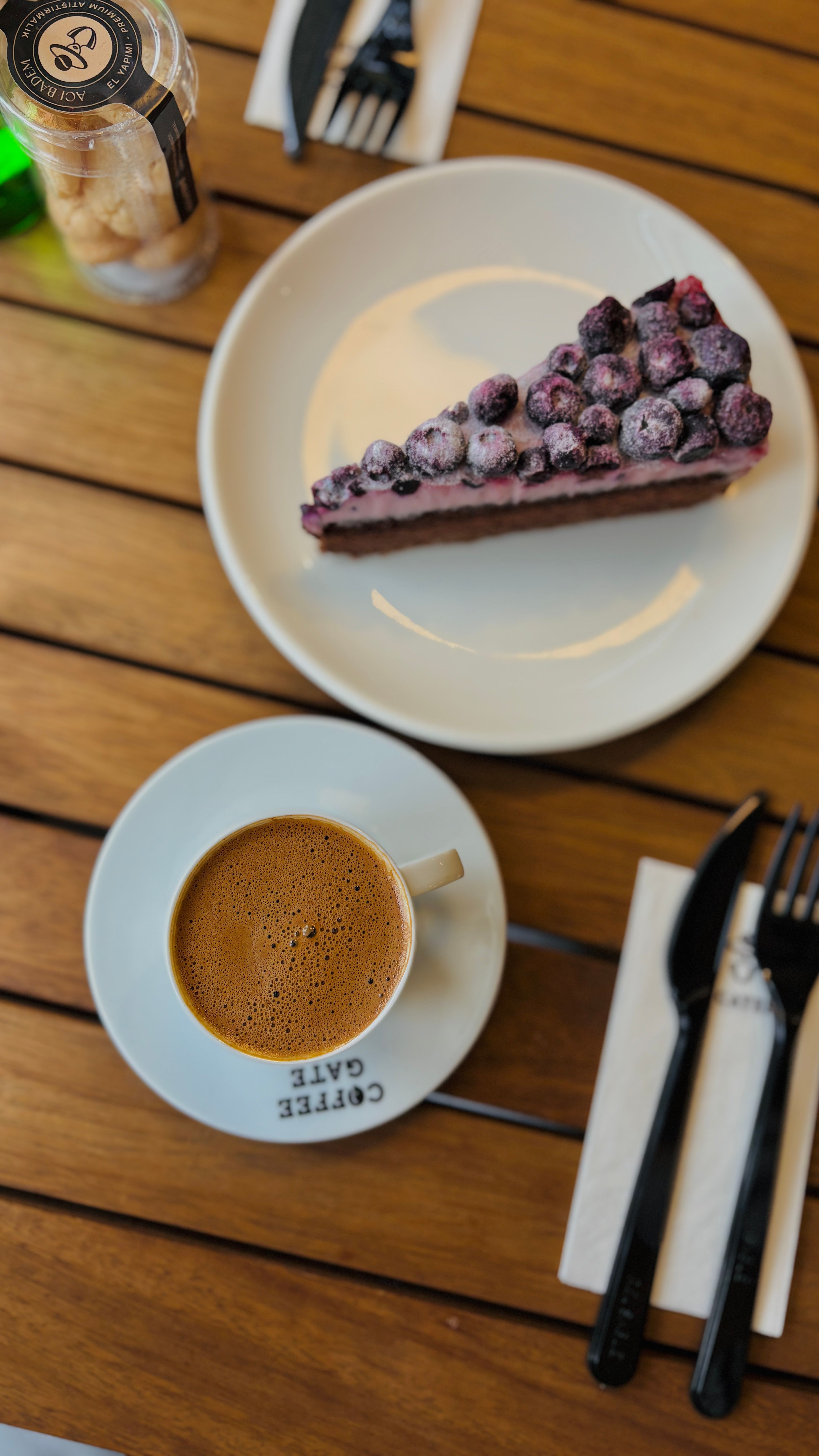 Top view of a coffee cup and blueberry cake slice on a wooden table setting.