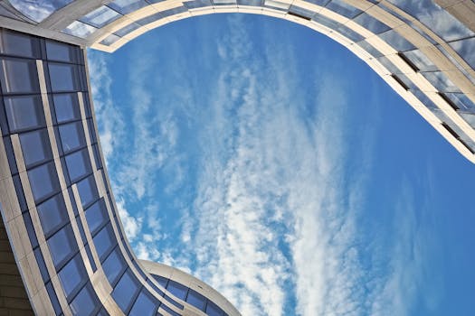现代摩天大楼的拱门设计在低角度视角下，映衬着清澈的蓝天和云层