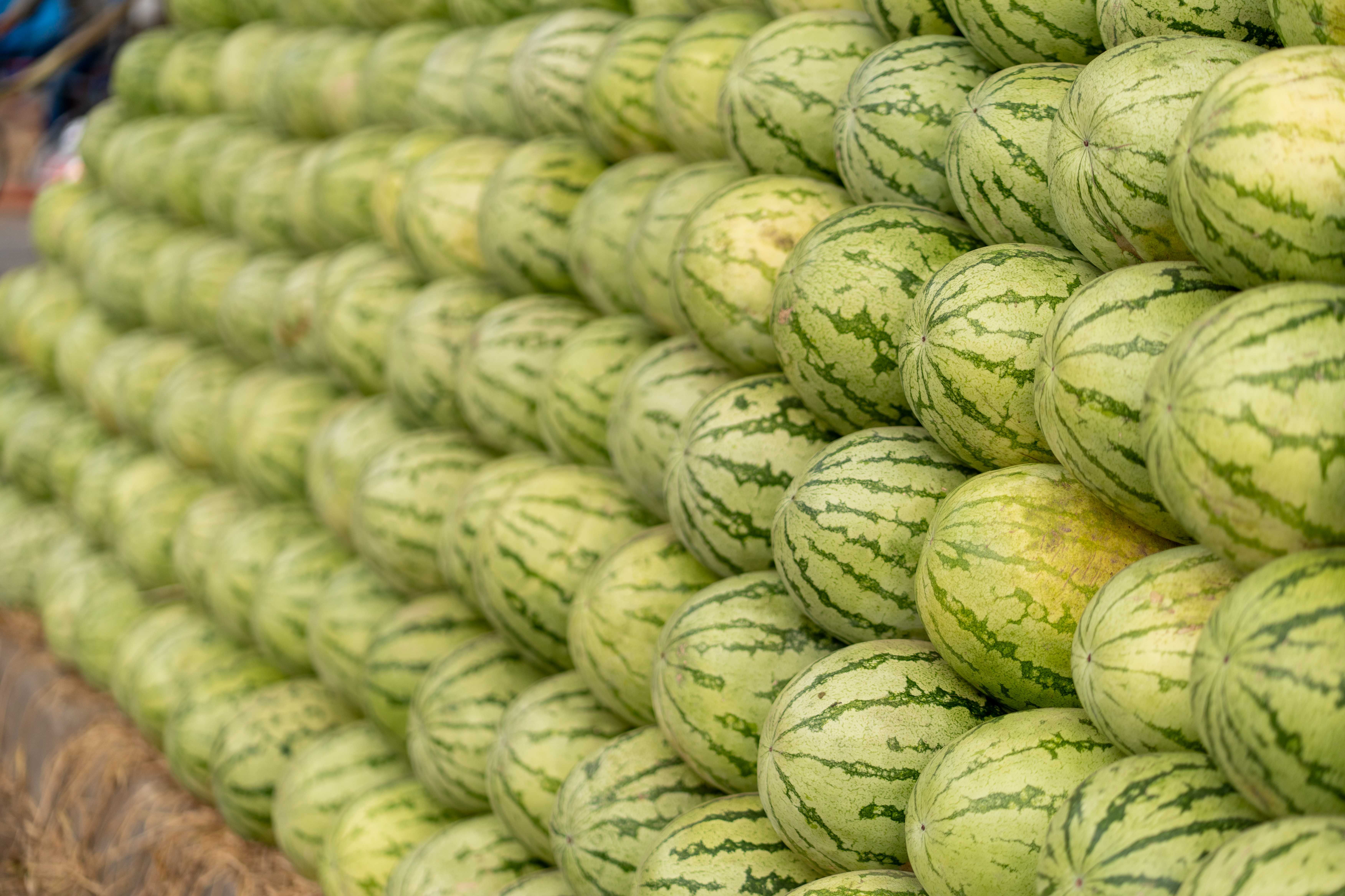 A neat stack of fresh watermelons arranged for sale in an outdoor market.