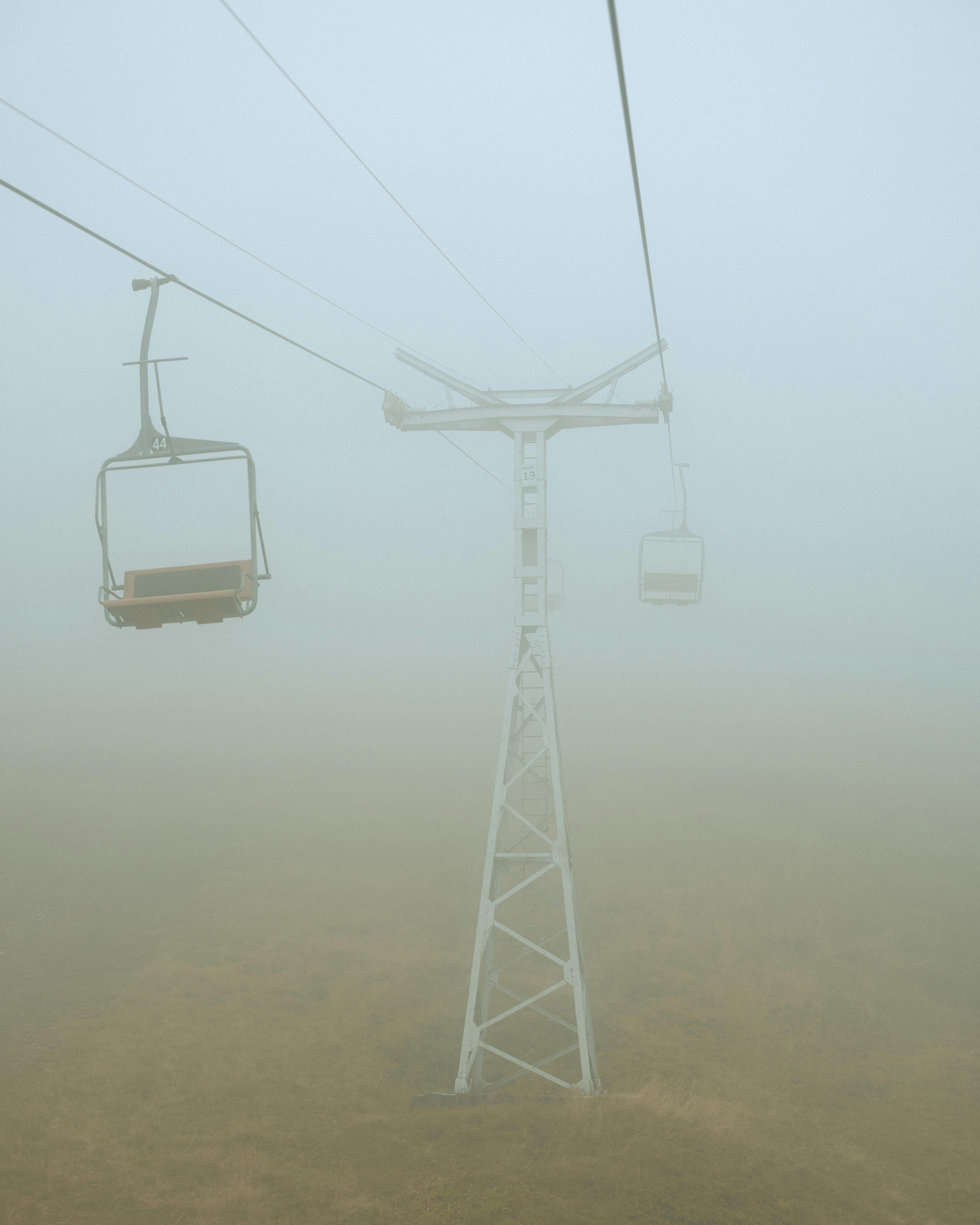 Eerie view of an empty chairlift disappearing into thick fog on a misty day.