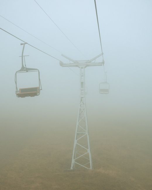 Eerie view of an empty chairlift disappearing into thick fog on a misty day.