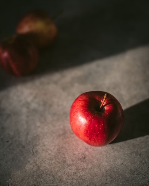 Free Single red apple in soft light casting shadow on a dark surface, evoking a moody atmosphere. Stock Photo