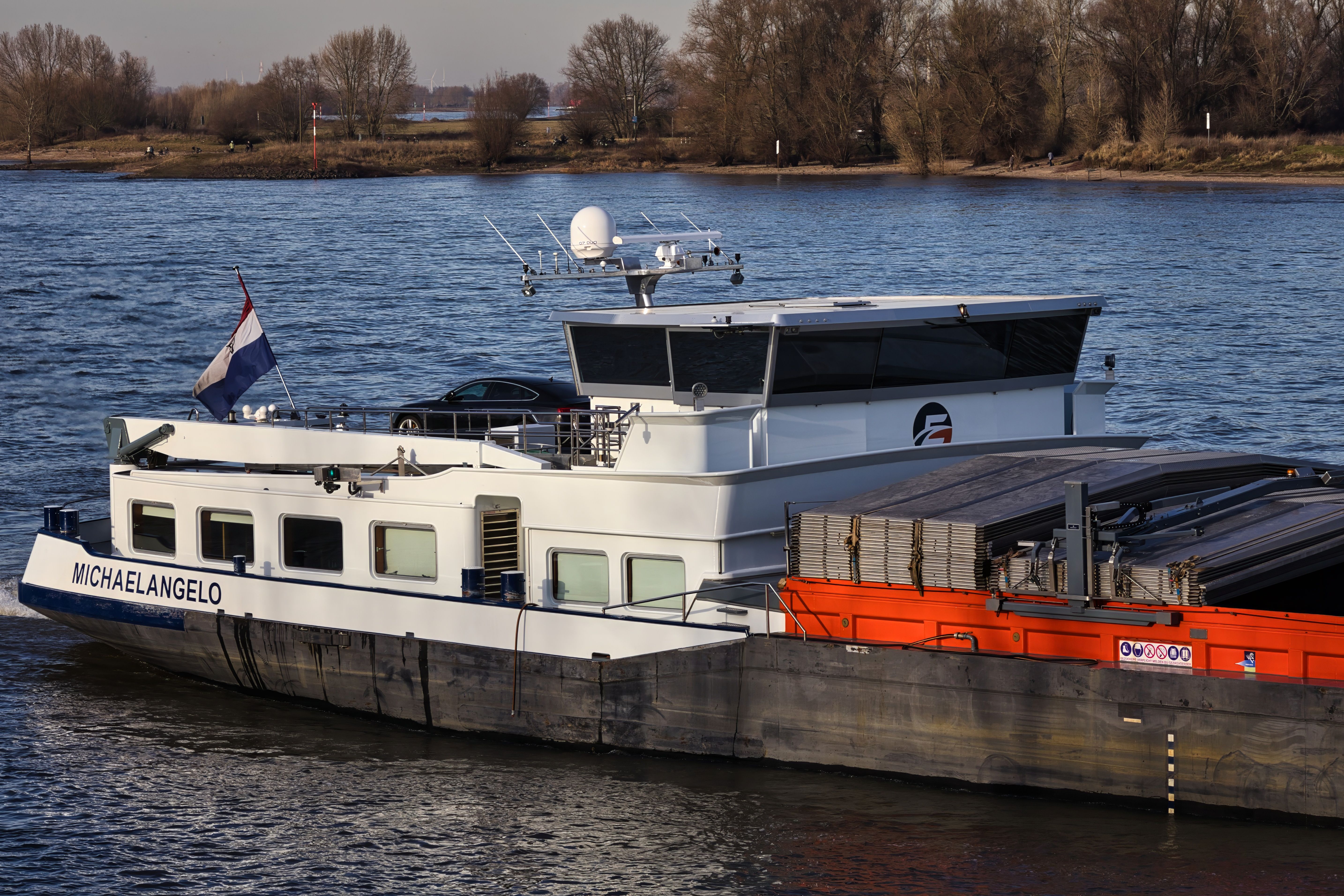 A cargo ship named Michaelangelo cruising the Rhine river on a sunny day.
