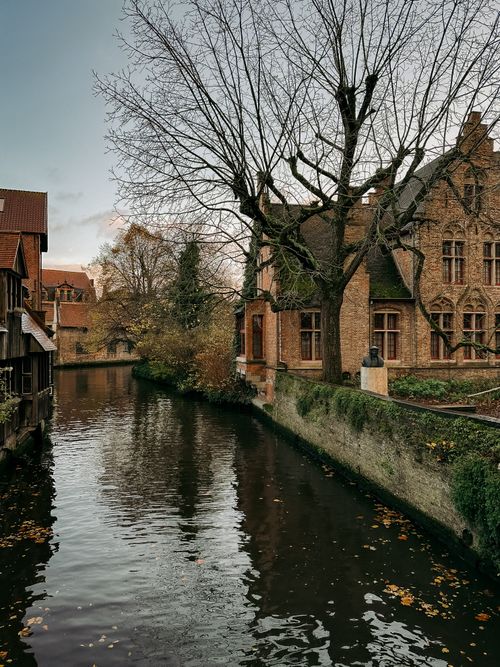 Free Serene autumn view of a canal in Bruges, Belgium with quaint architecture reflecting in calm waters. Stock Photo