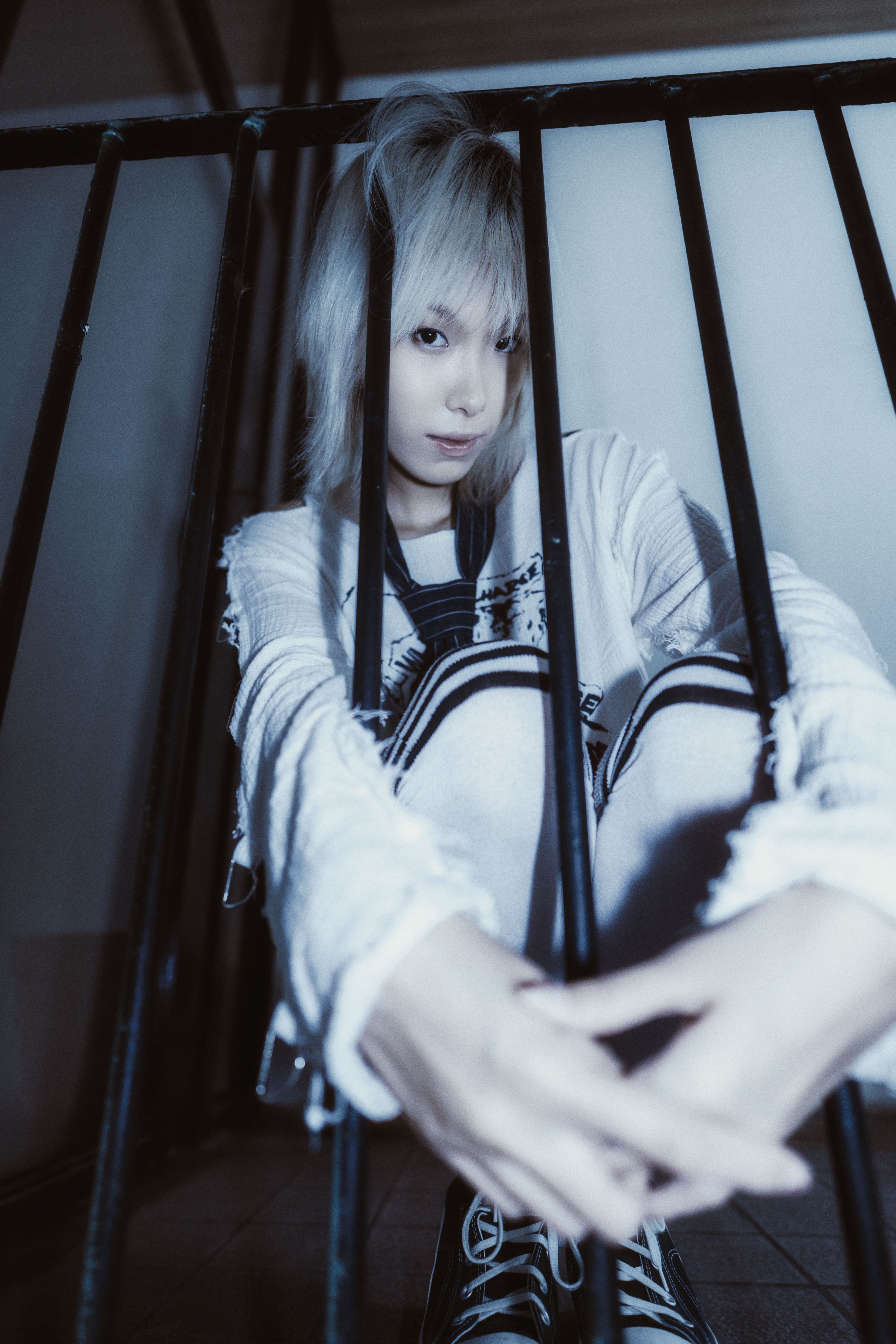 A young adult with a contemplative look behind bars, creating a moody atmosphere indoors.