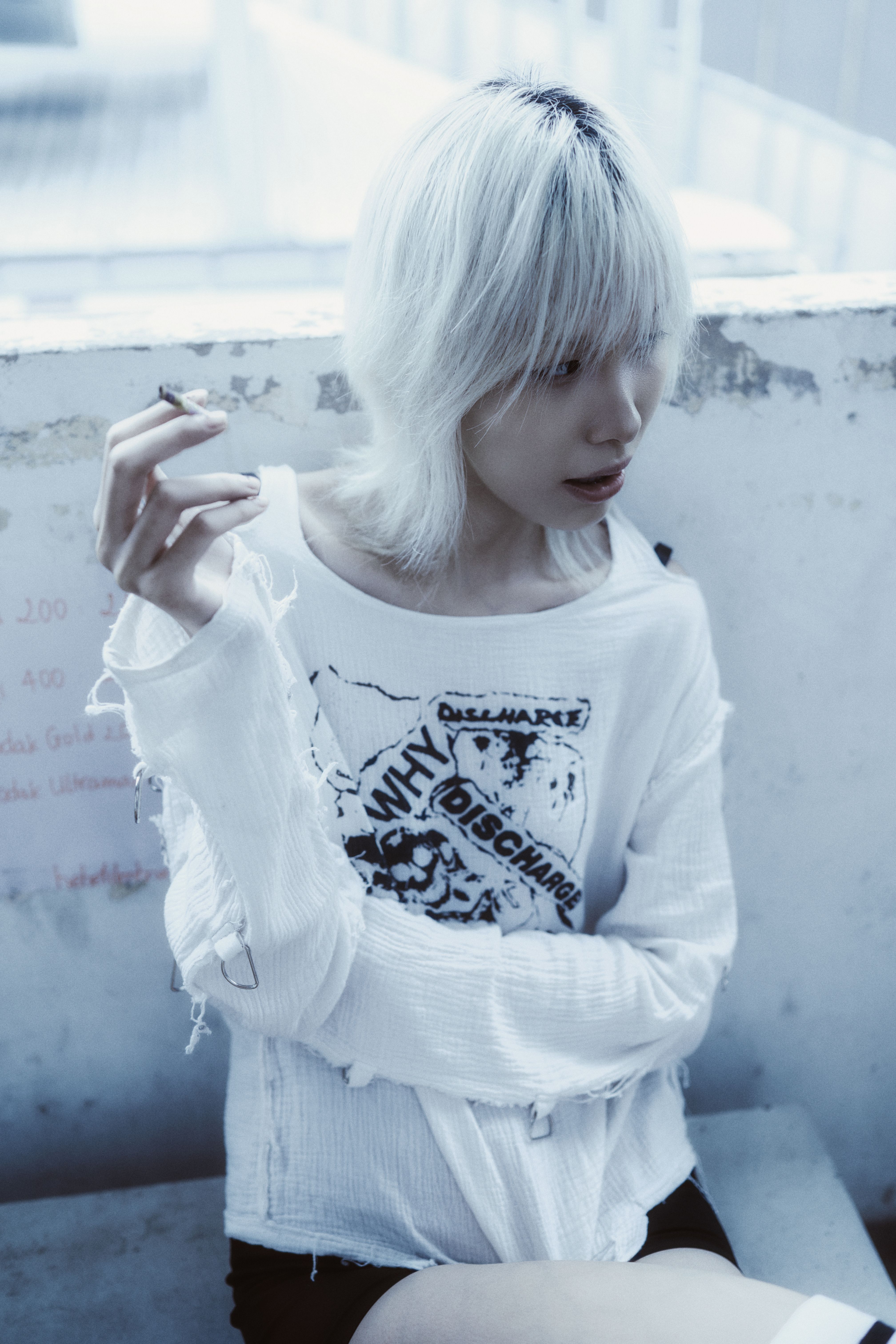 Edgy young adult with platinum hair, smoking in grunge attire on urban outdoor bench.