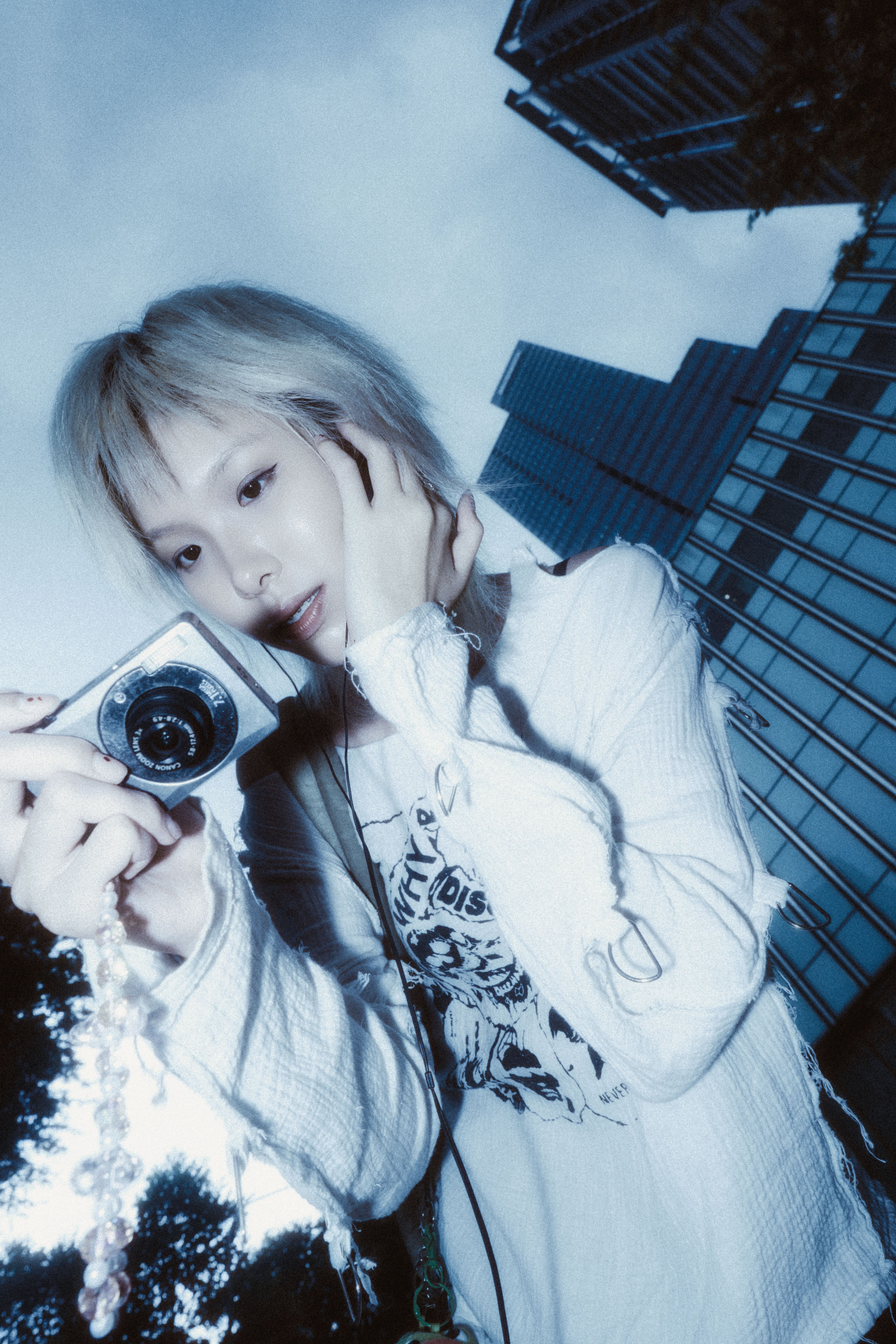 Stylish woman holds camera against urban skyscrapers in blue tone.