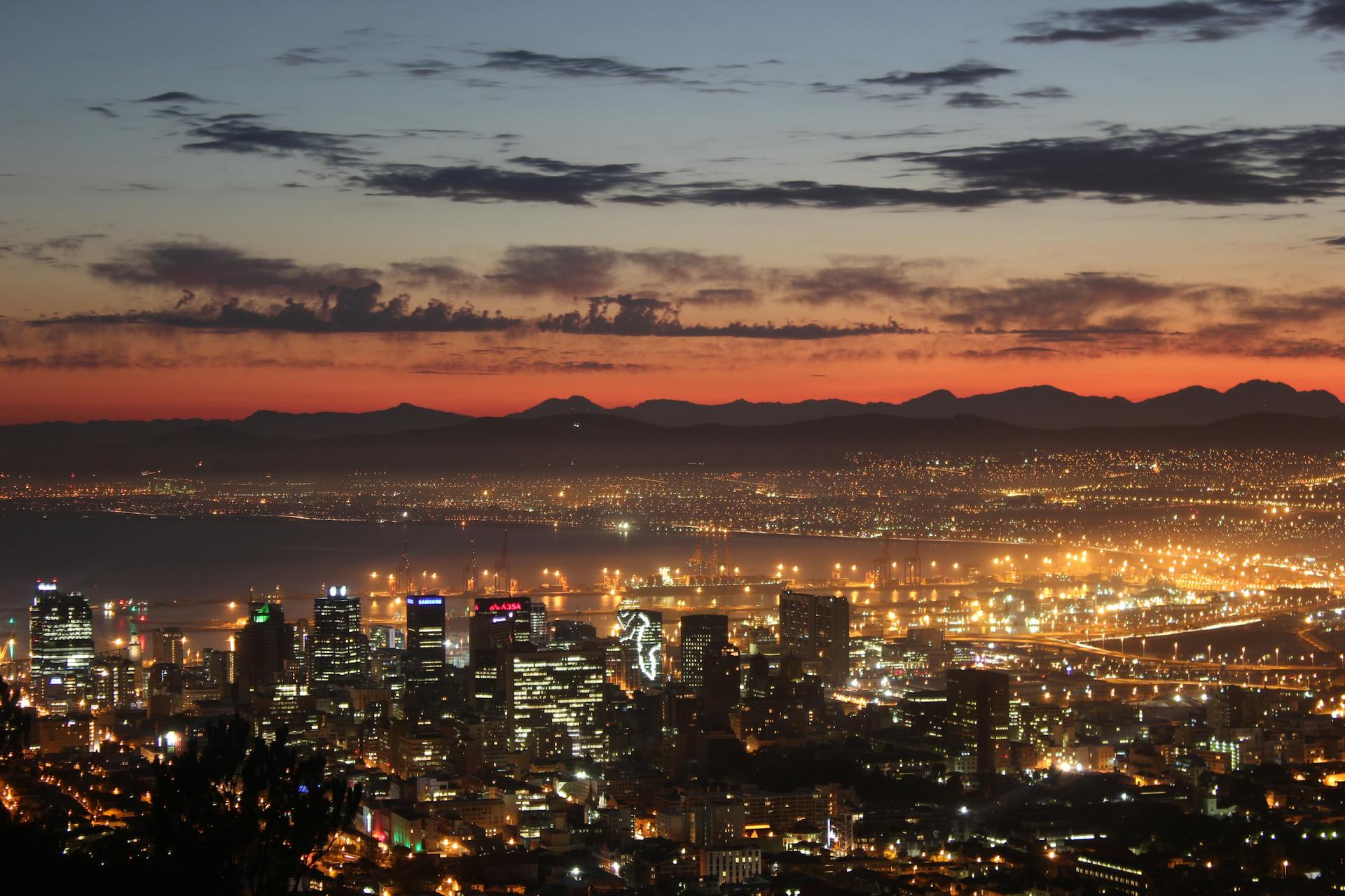 Vibrant cityscape of Cape Town at sunset, showcasing illuminated buildings and distant mountains.
