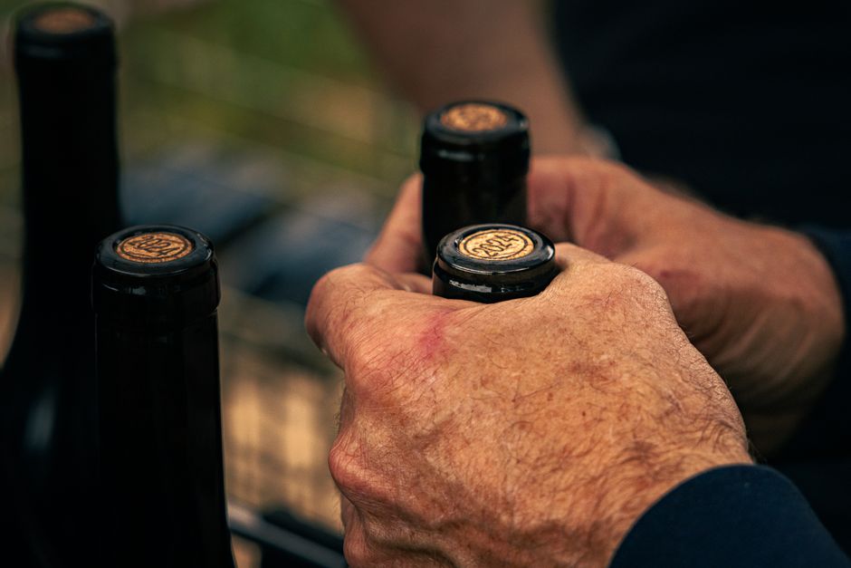 A double-lever hand corker pressing a cork straight down into the neck of a glass wine bottle on a kitchen counter.