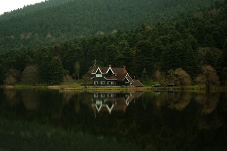 Dark timber lodge on a still lake shore backed by dense pine hillside — photo by ilayda 0700 on Pexels