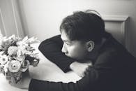 一个年轻人坐在黑白布景中，沉思着，身旁是插花