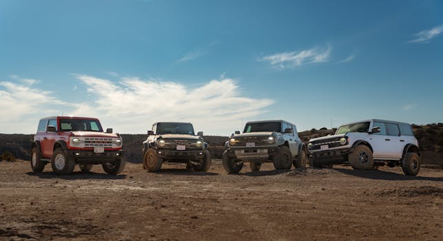 Four rugged off-road vehicles parked on dry rocky terrain under a clear blue sky.