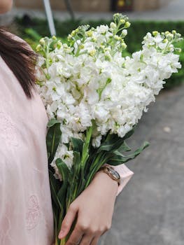 A woman holding a bouquet of fragrant white stock flowers outdoors, showcasing elegant floral beauty.