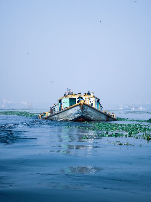 Free A rustic boat navigates a tranquil river surrounded by lush greenery under a clear blue sky. Stock Photo