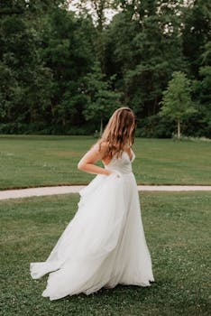 白天，身着白色婚纱的新娘在郁郁葱葱的公园里优雅地摆姿势拍照