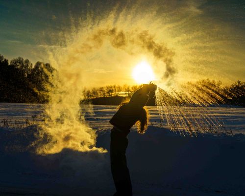 Free Silhouette of a person creating water splash effect against a sunset winter landscape. Stock Photo