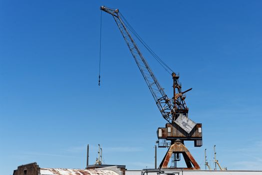 Rusty industrial crane set against a clear blue sky in a maritime setting.
