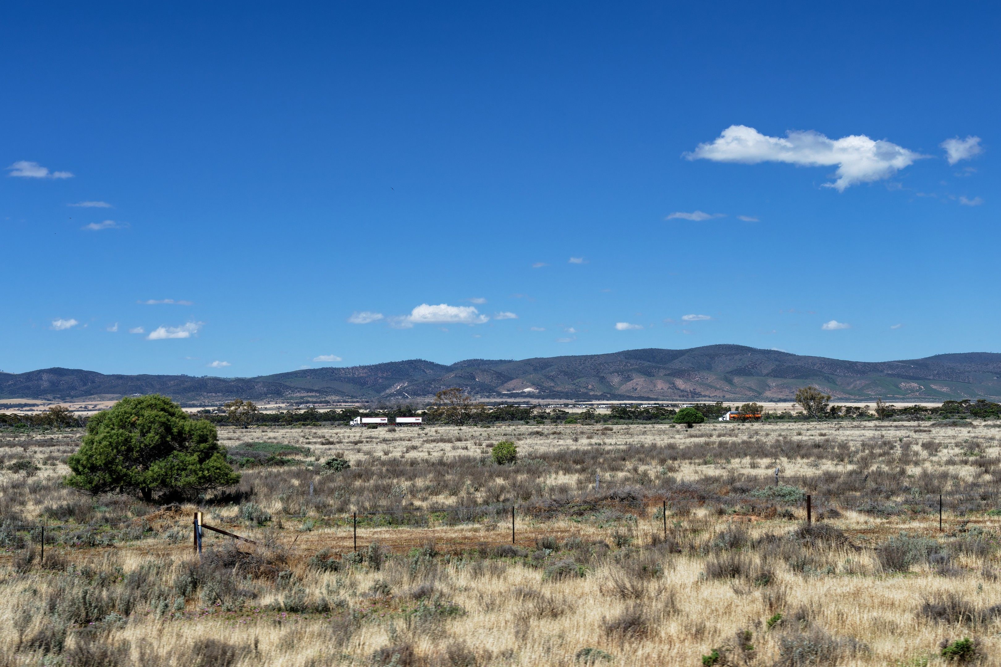 Expansive view of the Australian outback landscape under a clear blue sky. Hills in the distance with sparse vegetation.