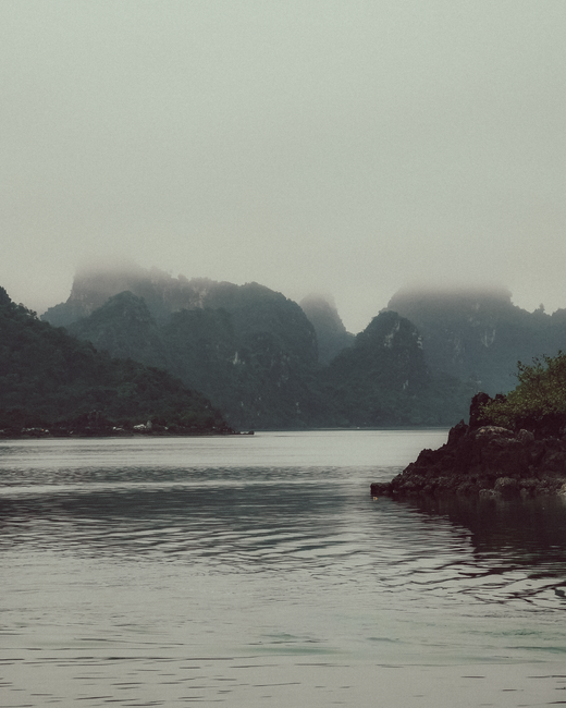 Serene misty landscape of Halong Bay with calm waters and striking limestone islands.