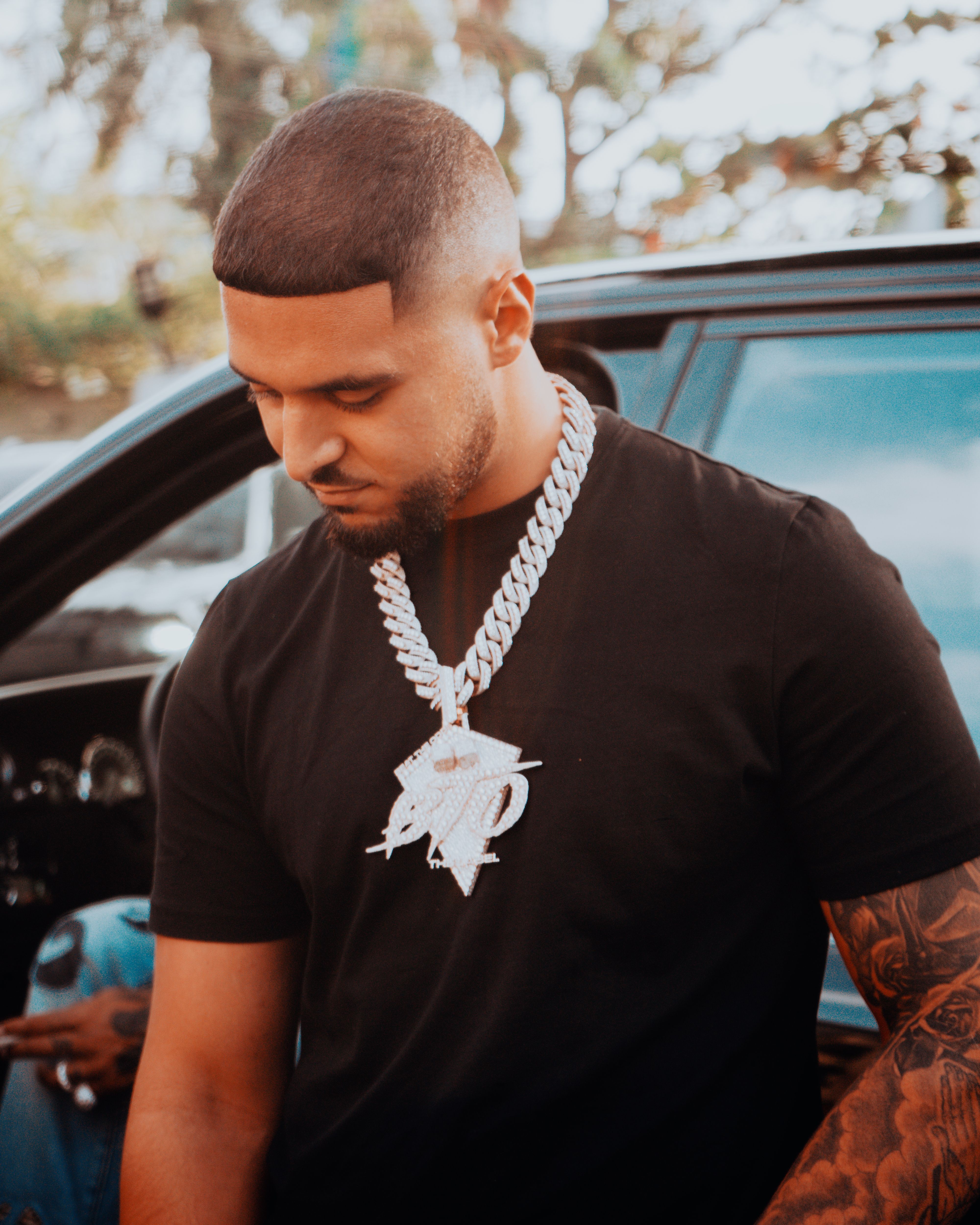 Confident young man wearing a bold chain necklace, standing next to a car outdoors.