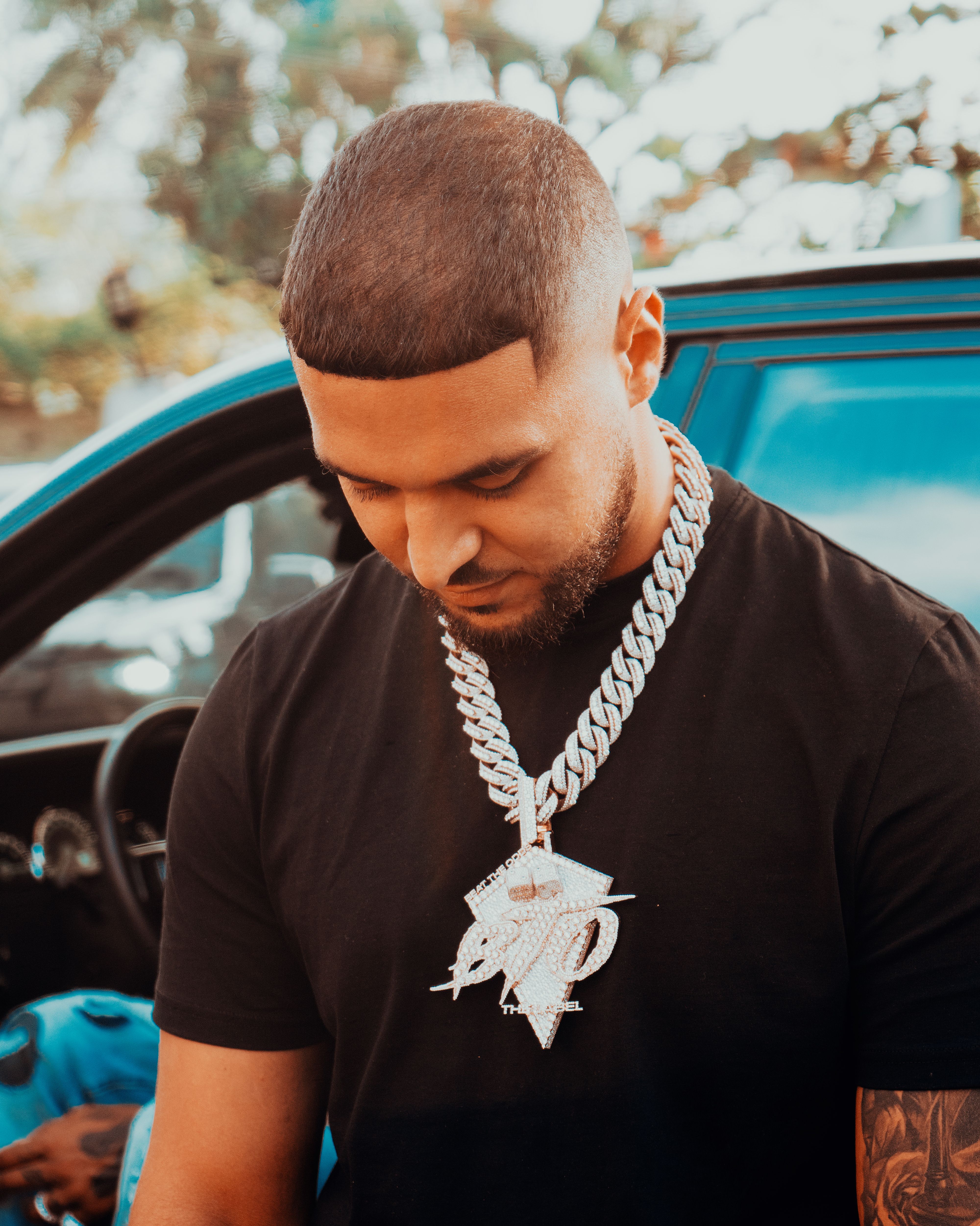 Man with a stylish diamond chain near a car, showcasing urban fashion and lifestyle.