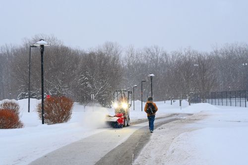 Free A person walks on a snowy path as a snowblower clears the way during a winter day. Stock Photo