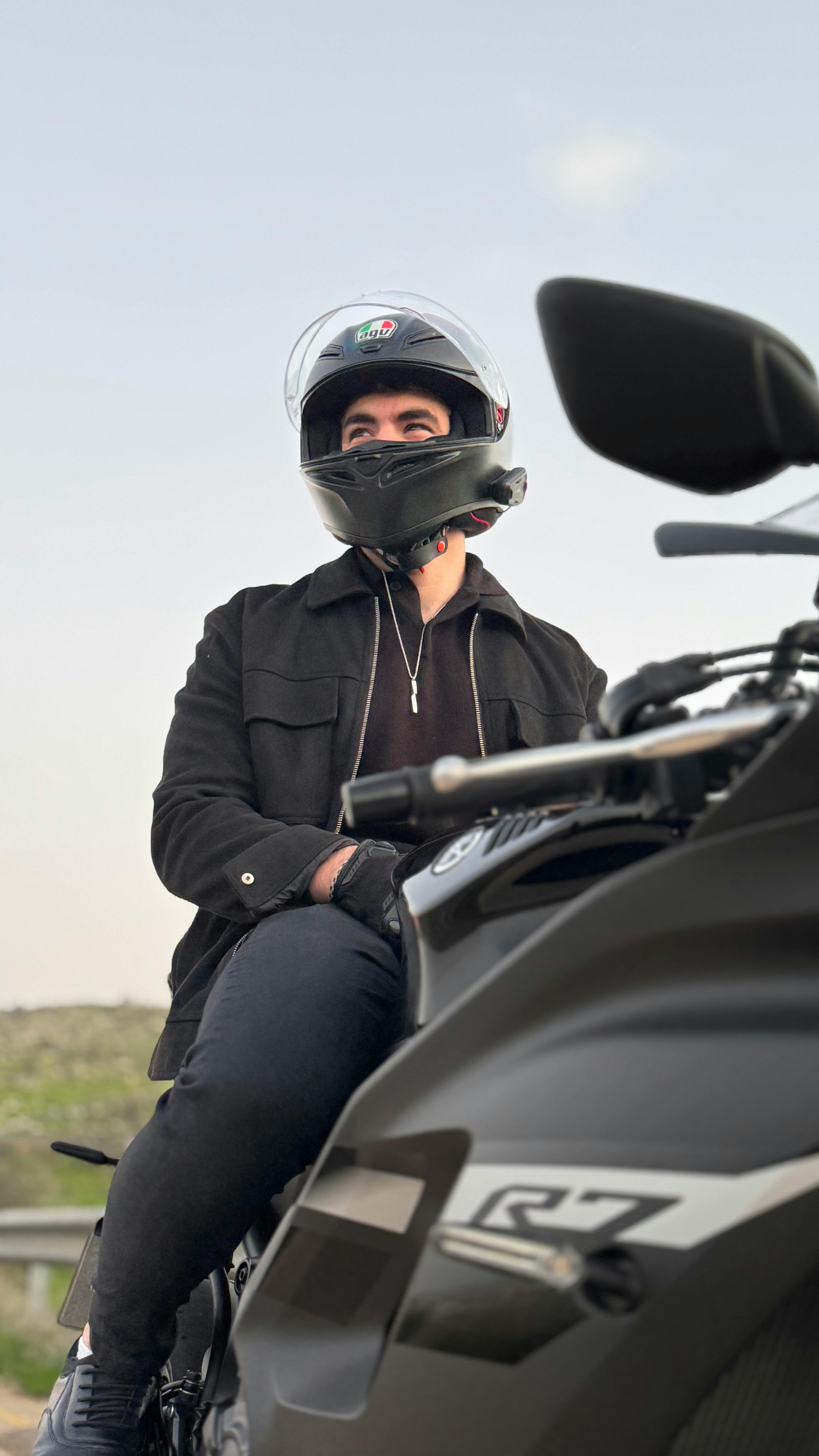 A motorcyclist wearing a helmet rides a black sports bike outdoors on a sunny day.