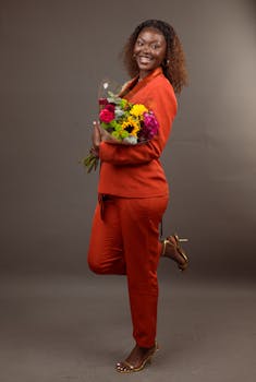 Cheerful woman in orange outfit holding a colorful bouquet, posing indoors.