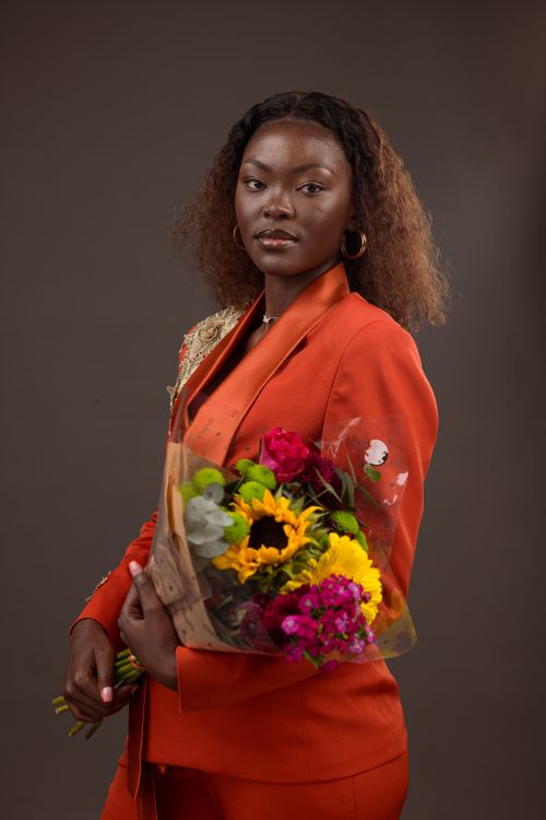Free Stylish woman in orange suit holding a vibrant bouquet of flowers, posing confidently in studio. Stock Photo