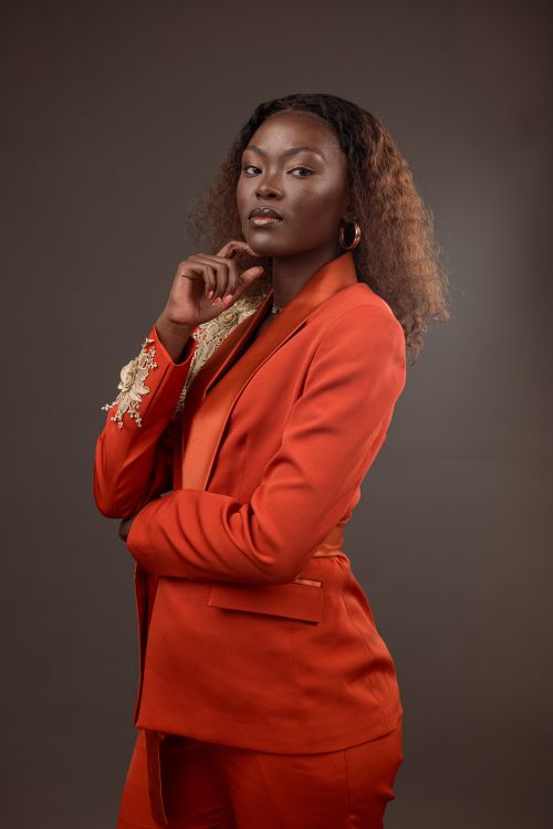 Free Confident woman posing in a vibrant orange suit with intricate detailing. Stock Photo