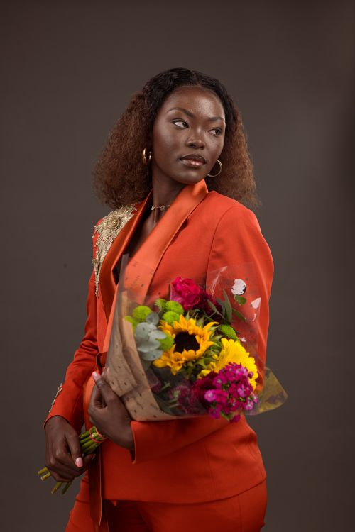 Free Stylish woman holding a bouquet, wearing an orange suit in a studio setting. Stock Photo