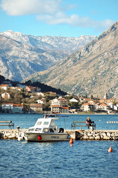Free White boat docked by the scenic bay in Montenegro with majestic mountain backdrop and quaint village. Stock Photo