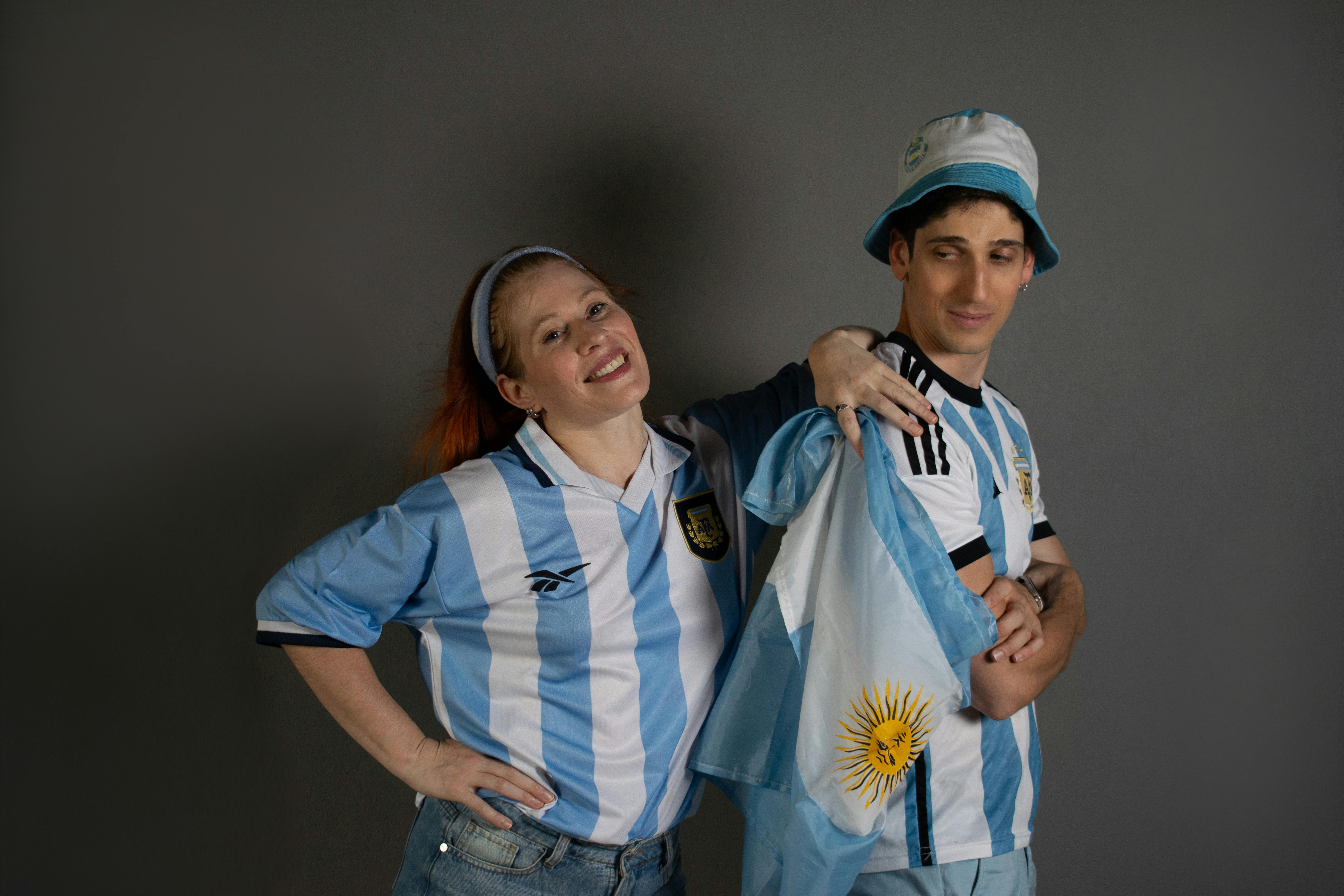 Two joyful Argentina soccer fans in team jerseys with a national flag, celebrating enthusiastically.