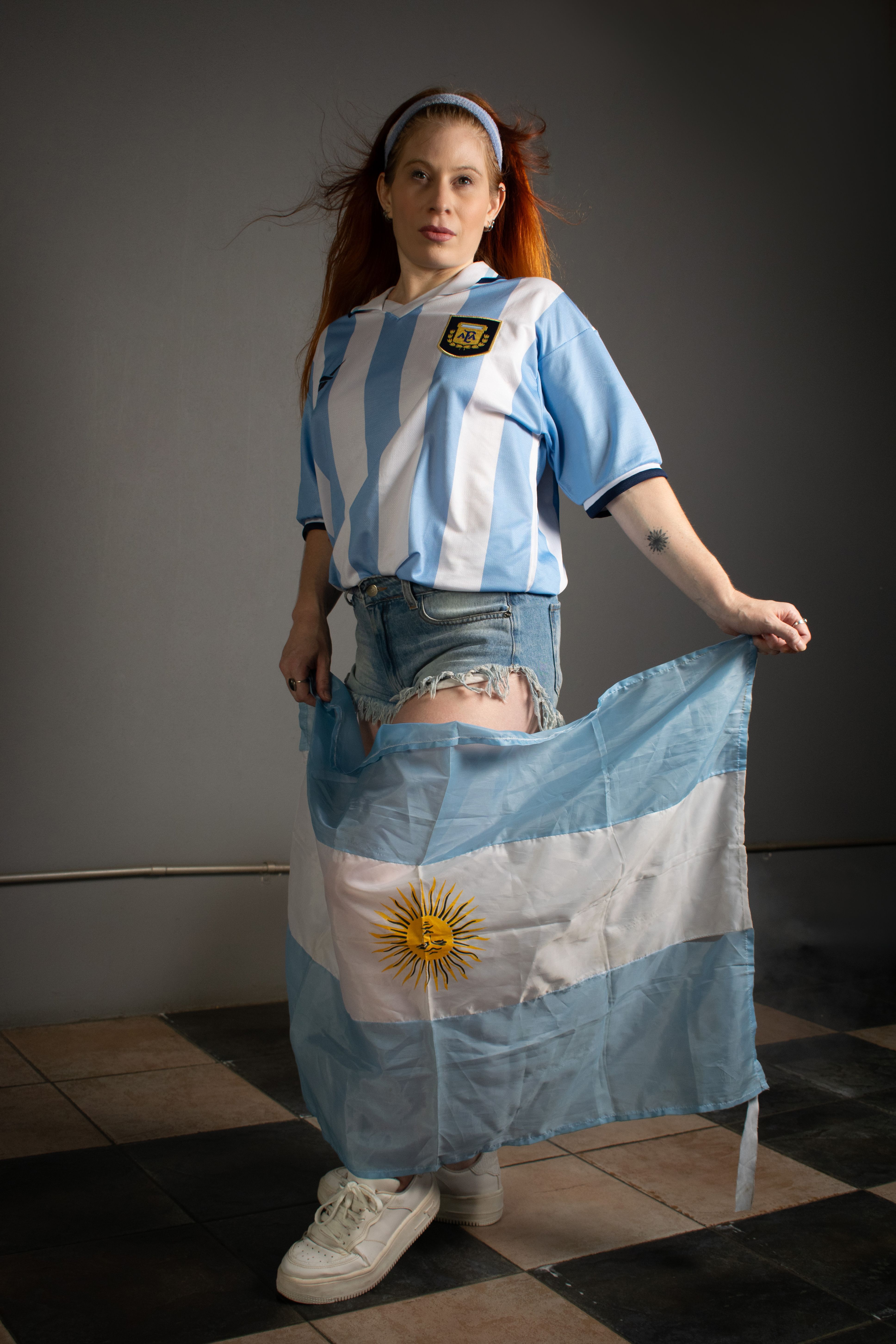 Young woman in Argentina jersey holding the national flag indoors.