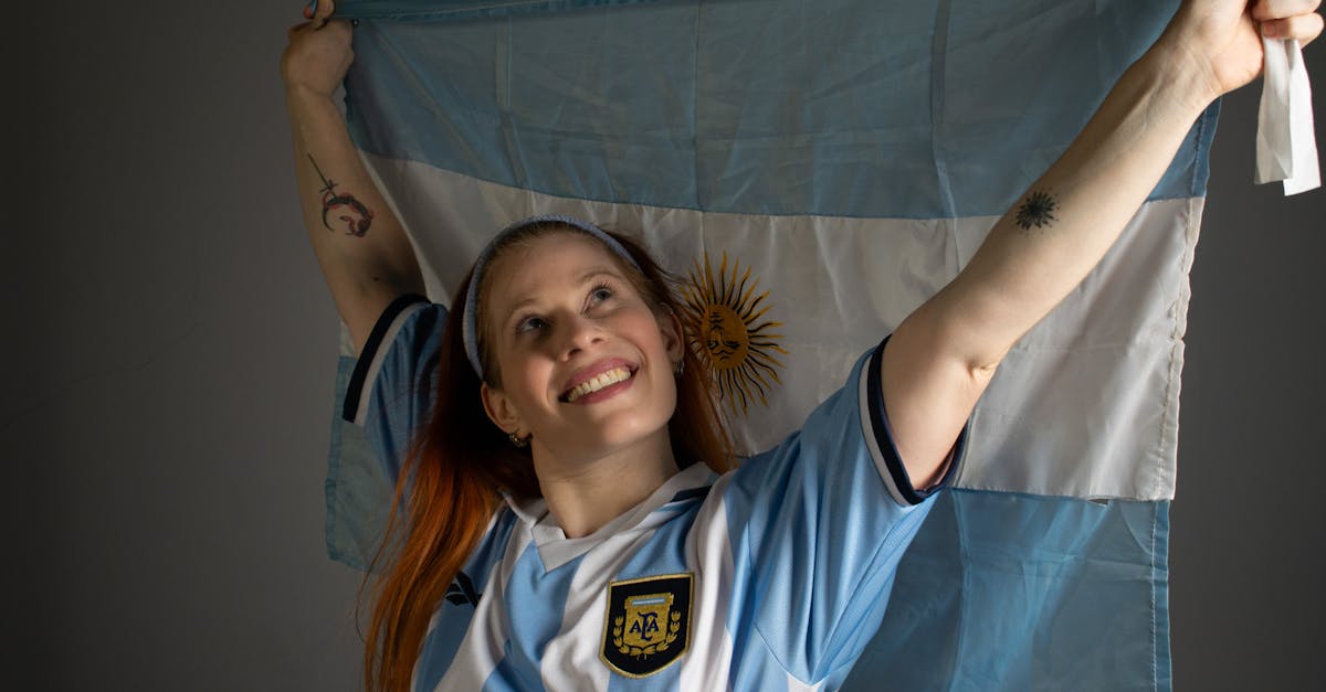 Smiling woman holding up the Argentina flag in celebration, wearing a blue and white jersey.