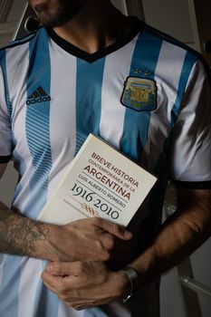 A person in an Argentina soccer jersey holding a history book about Argentina.