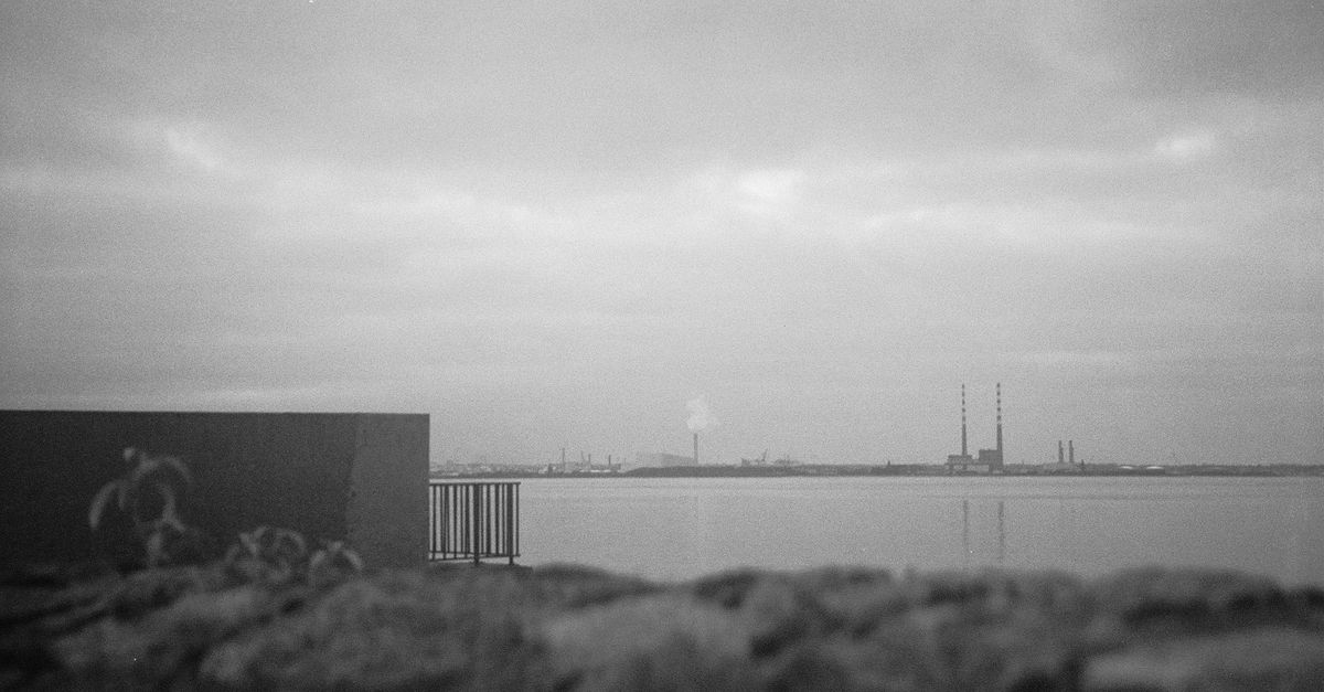 Black and white photo of a Dublin seaside with industrial structures under a cloudy sky.